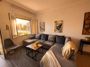 A living room with a sofa, a coffee table, a chair, and a window with a view. - Stylish Flat in Puerto Banús - Steps to Marina (Marbella)