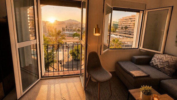 A modern living room with a balcony, a sofa, a chair, and a table with a candle. - Stylish Flat in Puerto Banús - Steps to Marina (Marbella)