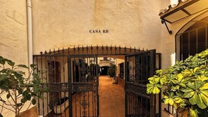 An arched entrance to a building labeled 'CASA RB' with a wrought iron gate, potted plants, and a tiled floor. - Stylish Flat in Puerto Banús - Steps to Marina (Marbella)