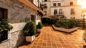 A courtyard with a tiled floor, potted plants, and a building with a sign reading 'Clinica Puerta J. Banos.' - Stylish Flat in Puerto Banús - Steps to Marina (Marbella)