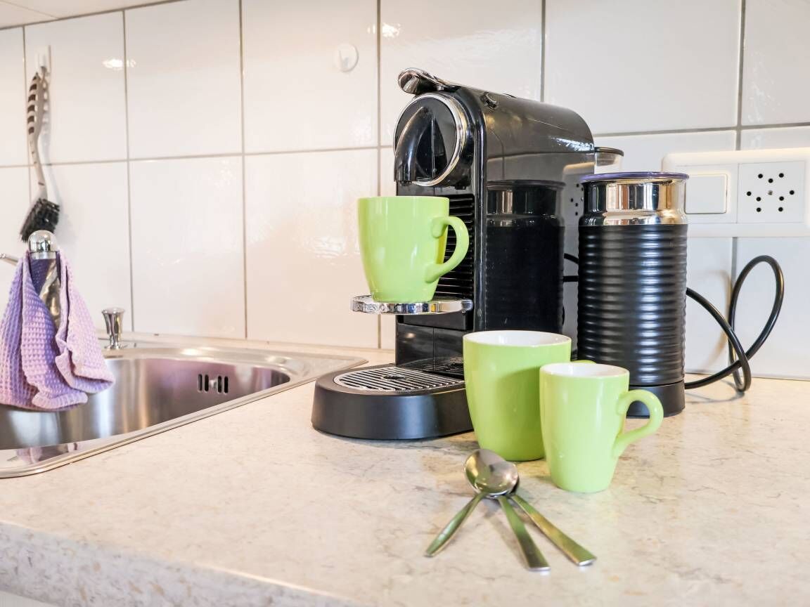 Eine Küche mit einer Kaffeemaschine, zwei grünen Tassen und einem Löffel auf der Arbeitsfläche.