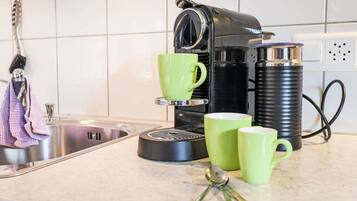 Eine Küche mit einer Kaffeemaschine, zwei grünen Tassen und einem Löffel auf der Arbeitsfläche.