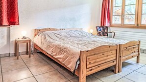 Ein Schlafzimmer mit einem hölzernen Bett, einem Nachttisch, einem Sessel und einem Fenster mit Vorhängen.