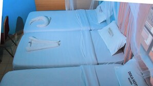Quarto de hotel com duas camas, cada uma com colcha e almofadas com a inscrição 'DEKA HOTEL NGARA'.