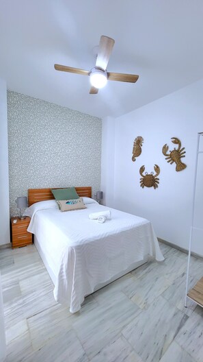 Une chambre à coucher comprenant un lit, une table de chevet, une lampe, un ventilateur de plafond et des œuvres d’art décoratives murales.