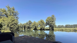 Ein ruhiger See mit Bäumen, deren Spiegelbild sich im Wasser zeigt, ein hölzerner Steg und ein klarer, blauer Himmel.