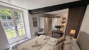 Ein Schlafzimmer mit großem Fenster, einem Bett mit Handtüchern, einem Sessel, einem Tisch mit Vase und einer Lampe.