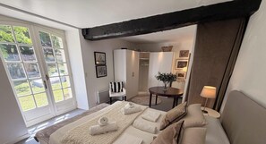 Une chambre avec une grande fenêtre, un lit avec des serviettes, une chaise, une table avec un vase et une lampe.