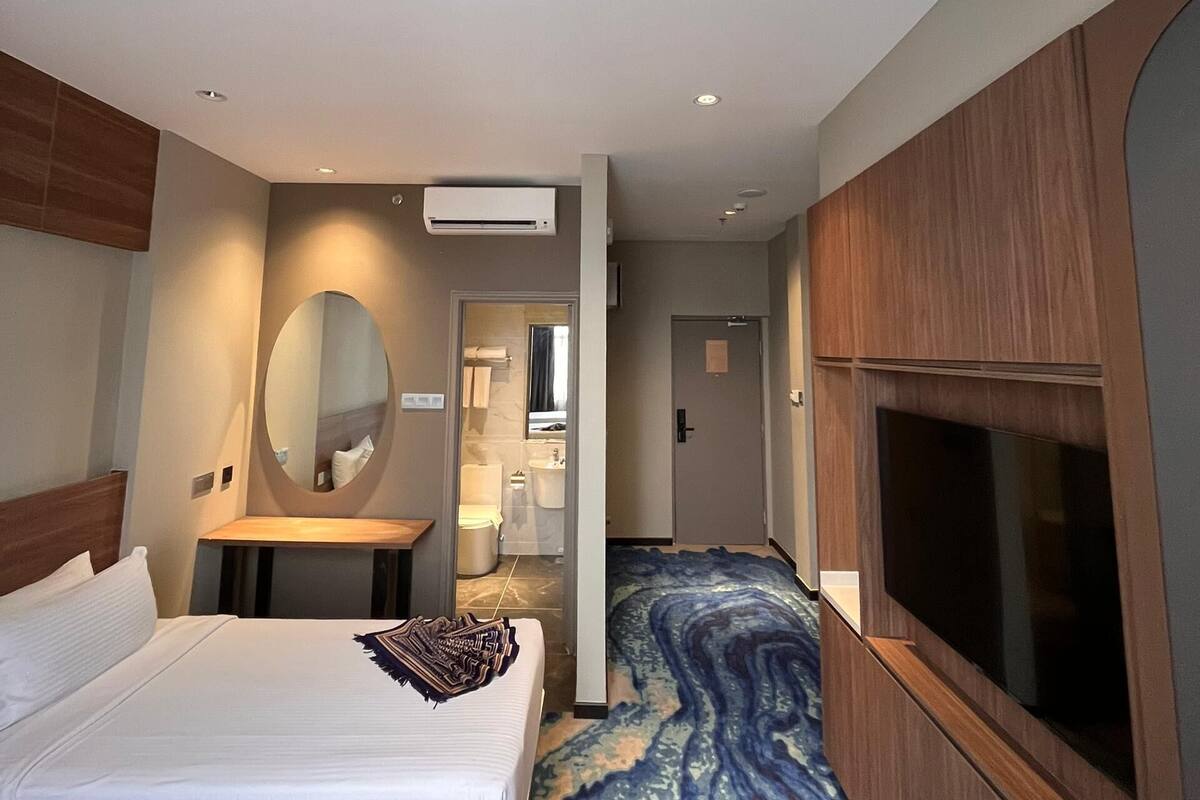 A hotel room with a bed, a TV, a mirror, and a bathroom visible through an open door.