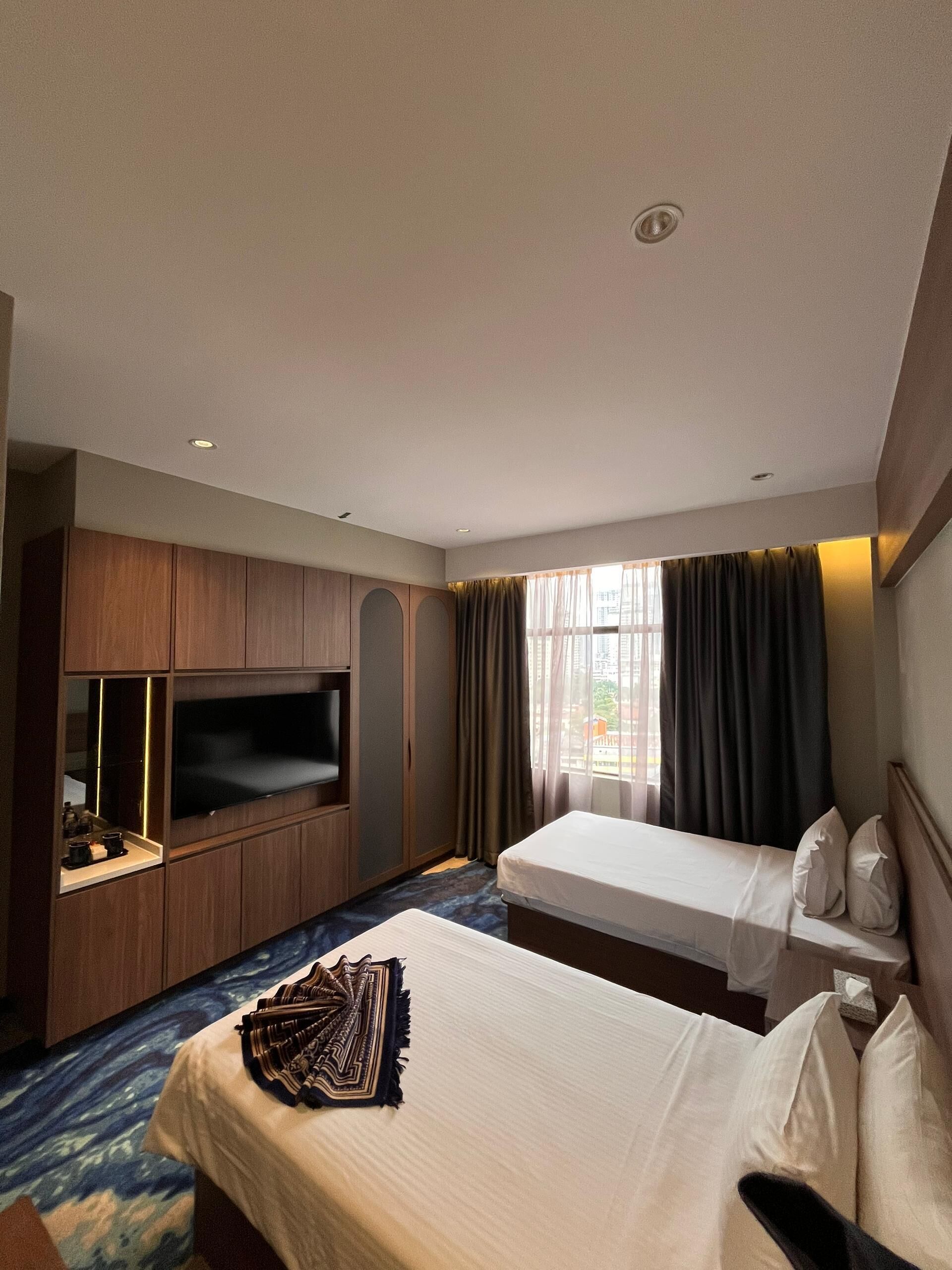 A hotel room with a bed, a TV, a minibar, and a window with curtains.