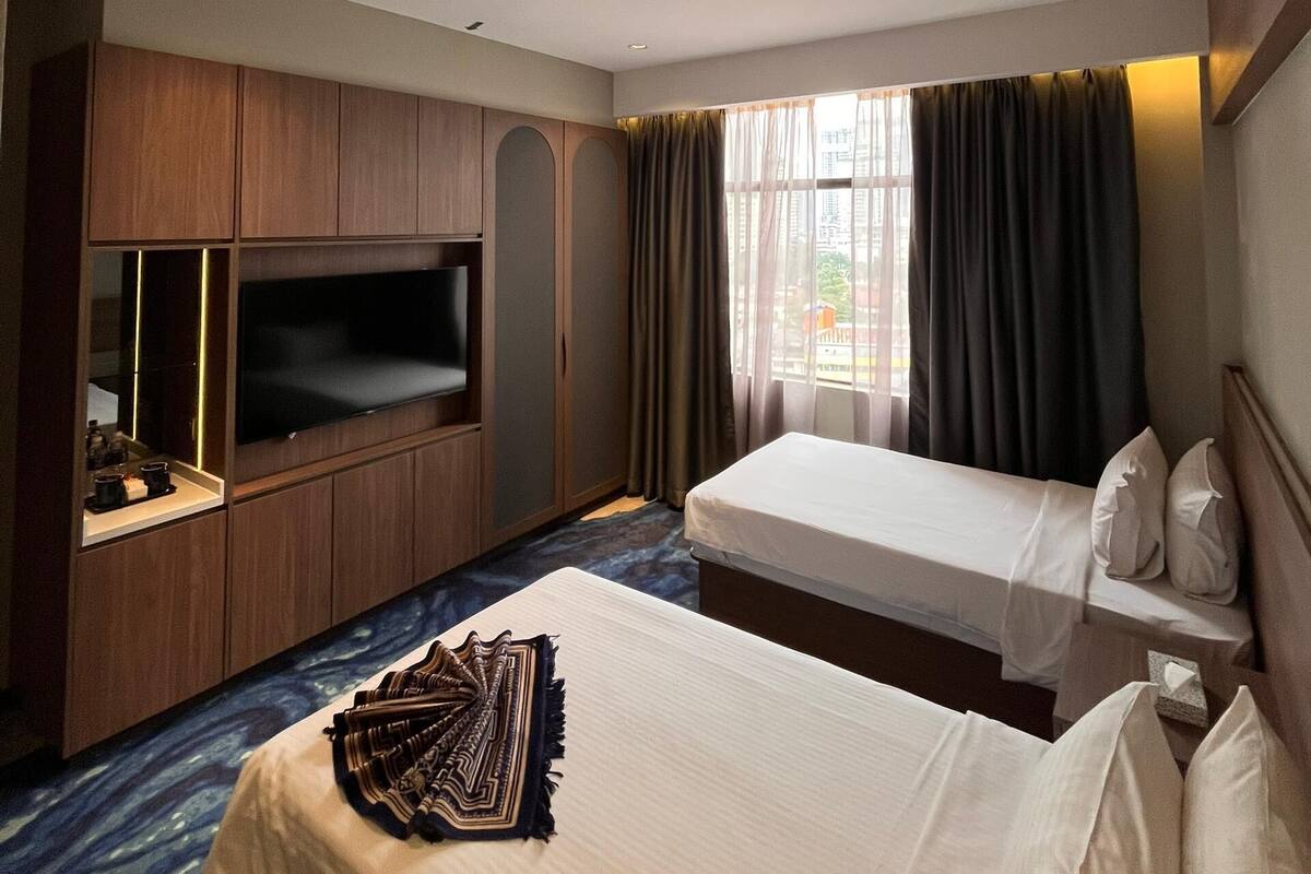 A hotel room with a bed, a TV, a minibar, and a window with curtains.