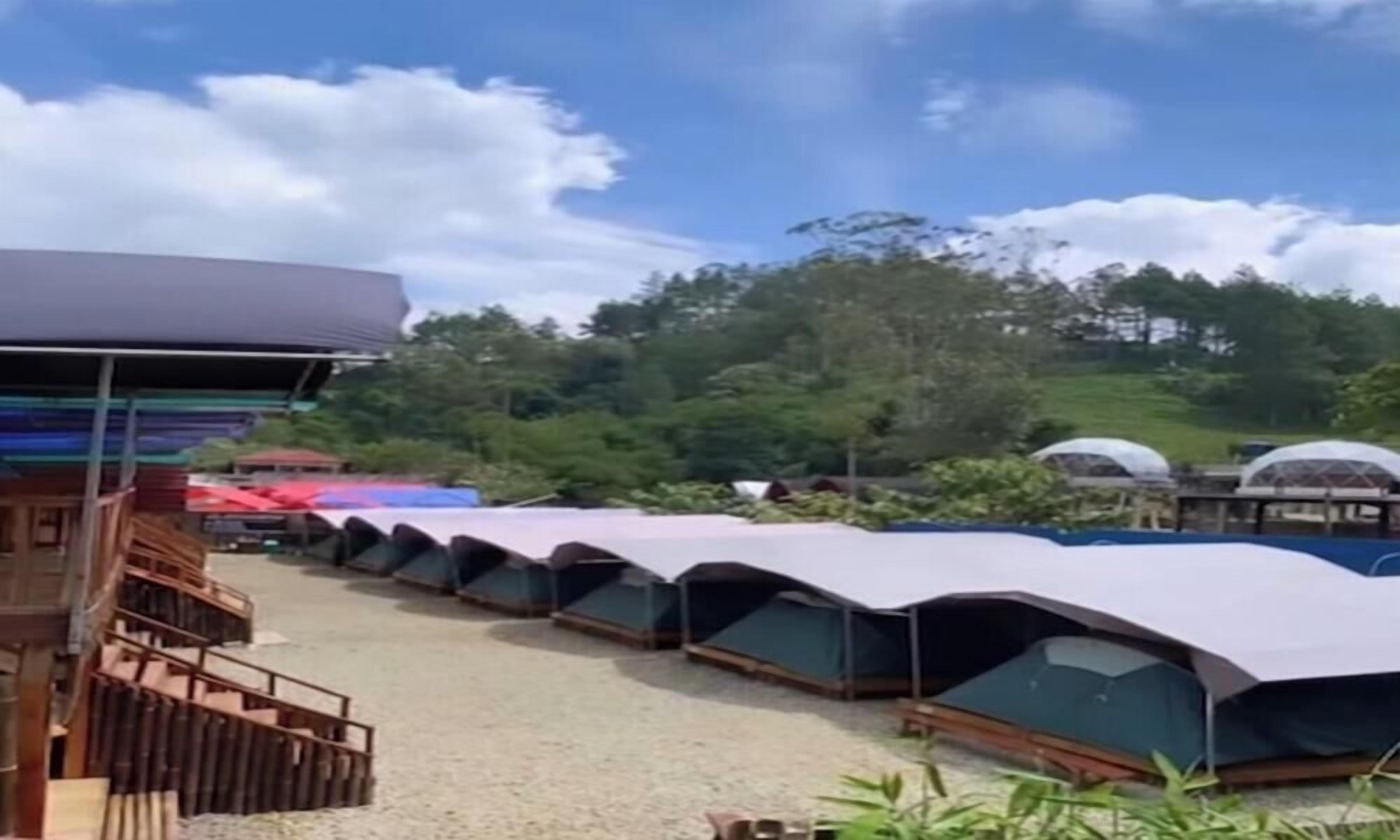 Une rangée de tentes dans un terrain de camping, avec un bâtiment sur la gauche.