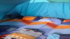 Uma tenda com toldo azul e uma cama com roupa de cama estampada.