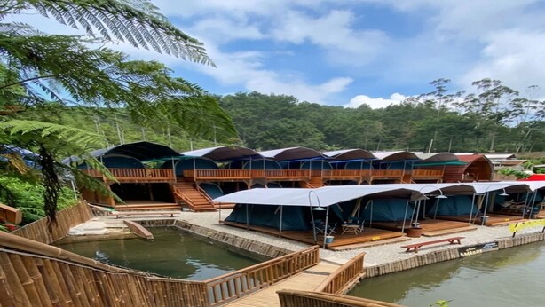 Uma série de passarelas de madeira que levam a bangalôs sobre a água, com piscina e área de deck.