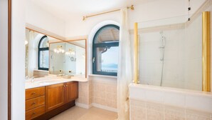 Une salle de bain avec une baignoire, une douche, un meuble-lavabo avec un miroir et une fenêtre donnant sur un paysage agréable.