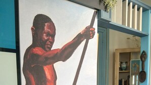 Quarto com uma pintura grande de um homem segurando uma lança, uma cadeira de madeira, uma estante e uma porta azul.