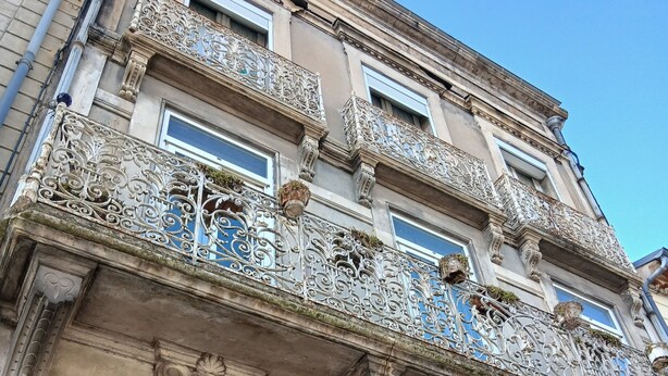 Um edifício com varandas ornamentadas, uma grande porta de entrada e uma placa azul com o número 8.