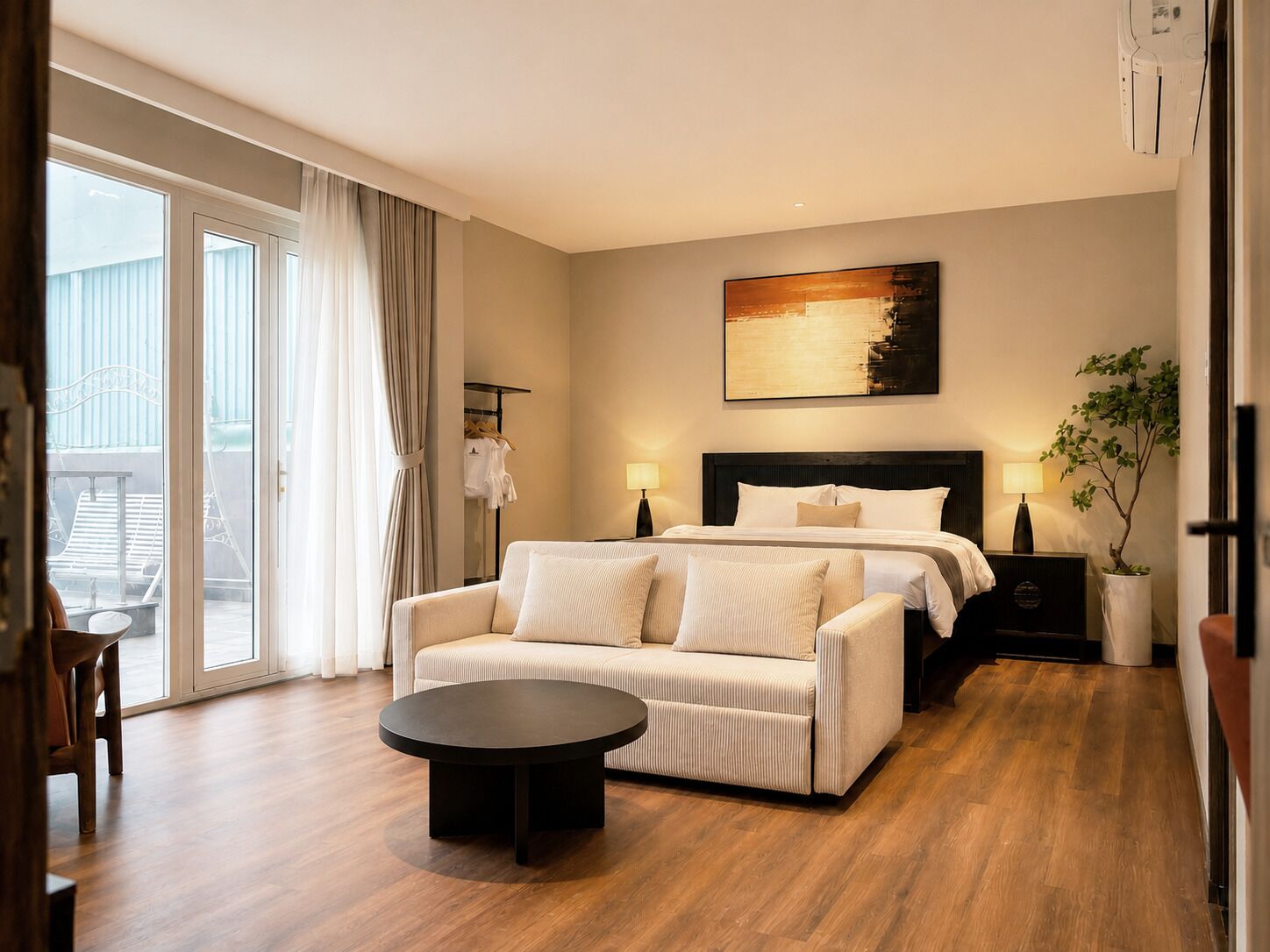 Een hotelkamer met een bed, een slaapbank, een ronde salontafel, een nachtkastje, een lamp, een schilderij en een potplant.