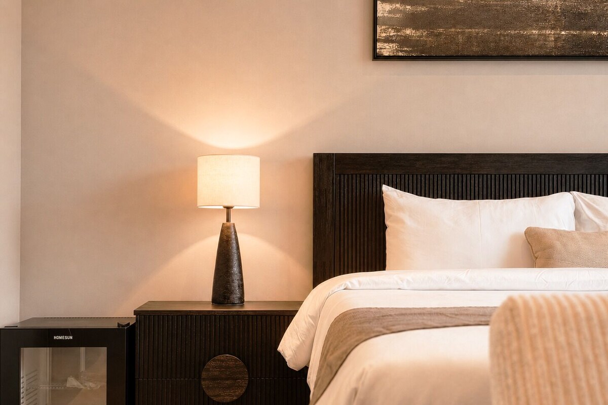 A hotel room with a bed, a nightstand with a lamp, and a refrigerator.