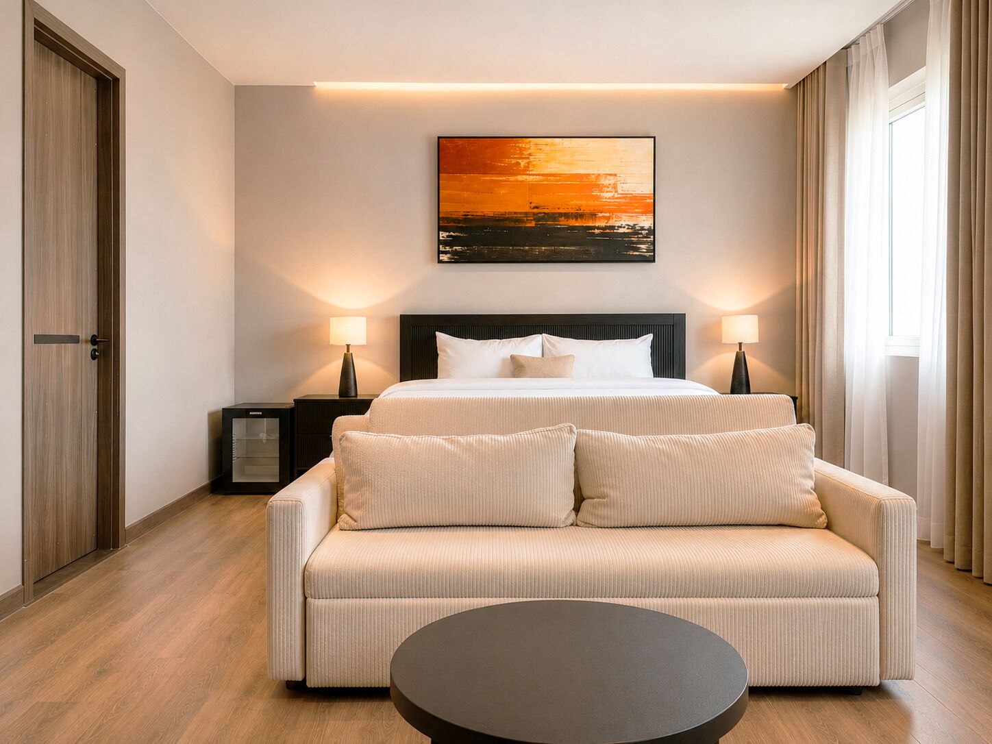 A hotel room with a bed, a sofa, a round table, and a painting on the wall.