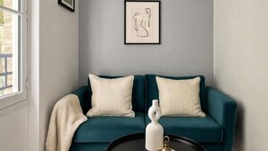 Ein blaugrünes Sofa mit zwei Kissen, ein schwarzer Couchtisch mit einer weißen Vase und ein gerahmtes abstraktes Kunstwerk an der Wand.