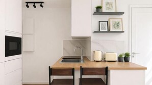 Eine moderne Küche mit weißen Schränken, einer Holz Arbeitsplatte, zwei Barhocker, einer Spüle und einer Mikrowelle.