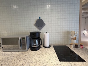 Eine Küche mit Kaffeemaschine, Papierhandtuchhalter, Mikrowelle und einer schwarzen Matte auf der Arbeitsfläche.