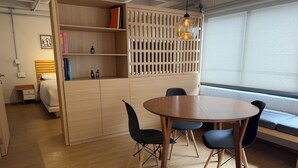 A modern room with a wooden desk, a round table with chairs, a bed, and a window with blinds. - Modern 1BR in Juárez with fast WiFi, great natural light, a comfortable queen bed, a fully equipped kitchen, and a luxury bathroom. Perfect for couples or solo travelers seeking comfort, style, and a prime location in Mexico City. (Cuauhtémoc)