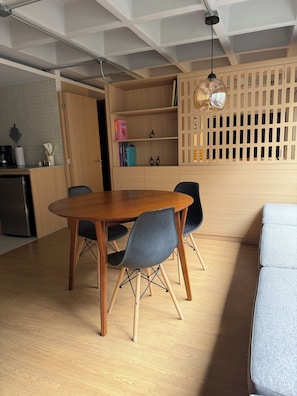 Ein Essbereich mit Holztisch und -stühlen, ein Küchenbereich mit Kühlschrank und eine Holzabtrennung mit Regalen.