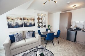 A modern living room with a sofa, a dining table with chairs, a kitchen area, and artwork on the walls. - Queensferry Collection - Residence 9 (Derby)