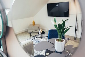 A modern living room with a round coffee table, a potted plant, a blue chair, and a flat-screen TV mounted on the wall. - Queensferry Collection - Residence 9 (Derby)