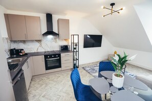 A modern kitchen with a microwave, oven, and a built-in range hood. There is a dining area with a table and chairs, and a potted plant on the table. - Queensferry Collection - Residence 9 (Derby)
