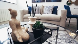 Ett modernt vardagsrum med ett soffbord i glas, en skulptur, en krukväxt och en soffa med kuddar.