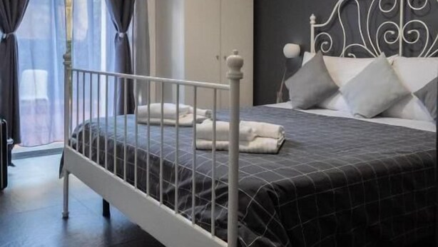 Un dormitorio con estructura de cama metálica, cabecera oscura, armario blanco y ventana con cortinas.