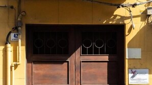 Puertas de madera dobles con una celosía metálica, una pared amarilla y un cartel con una cruz roja.