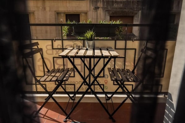 Ein Balkon mit Tisch und Stühlen, einer Topfpflanze und Blick auf ein Gebäude.