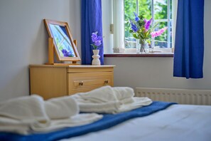 Ein Schlafzimmer mit einem Bett, einem Nachttisch mit einem gerahmten Bild und einer Blumenvase sowie einem Fenster mit Vorhängen.