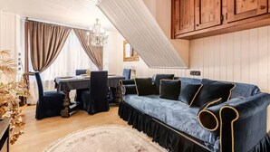 Um quarto com um sofá azul escuro, armários de madeira, uma mesa de jantar e um candelabro.