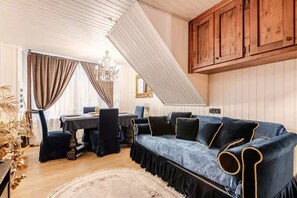 A room with a dark blue sofa, wooden cabinets, a dining table, and a chandelier. - [Courmayeur City Center] Imperial Elegance (Courmayeur)