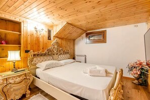 A bedroom with a wooden ceiling, a bed with ornate headboard, a nightstand with a lamp, and a radiator. - [Courmayeur City Center] Imperial Elegance (Courmayeur)