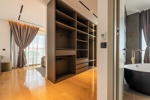 Et moderne badeværelse med et fristående badekar, et walk-in closet med mange hylder og et stort vindue med gardiner.