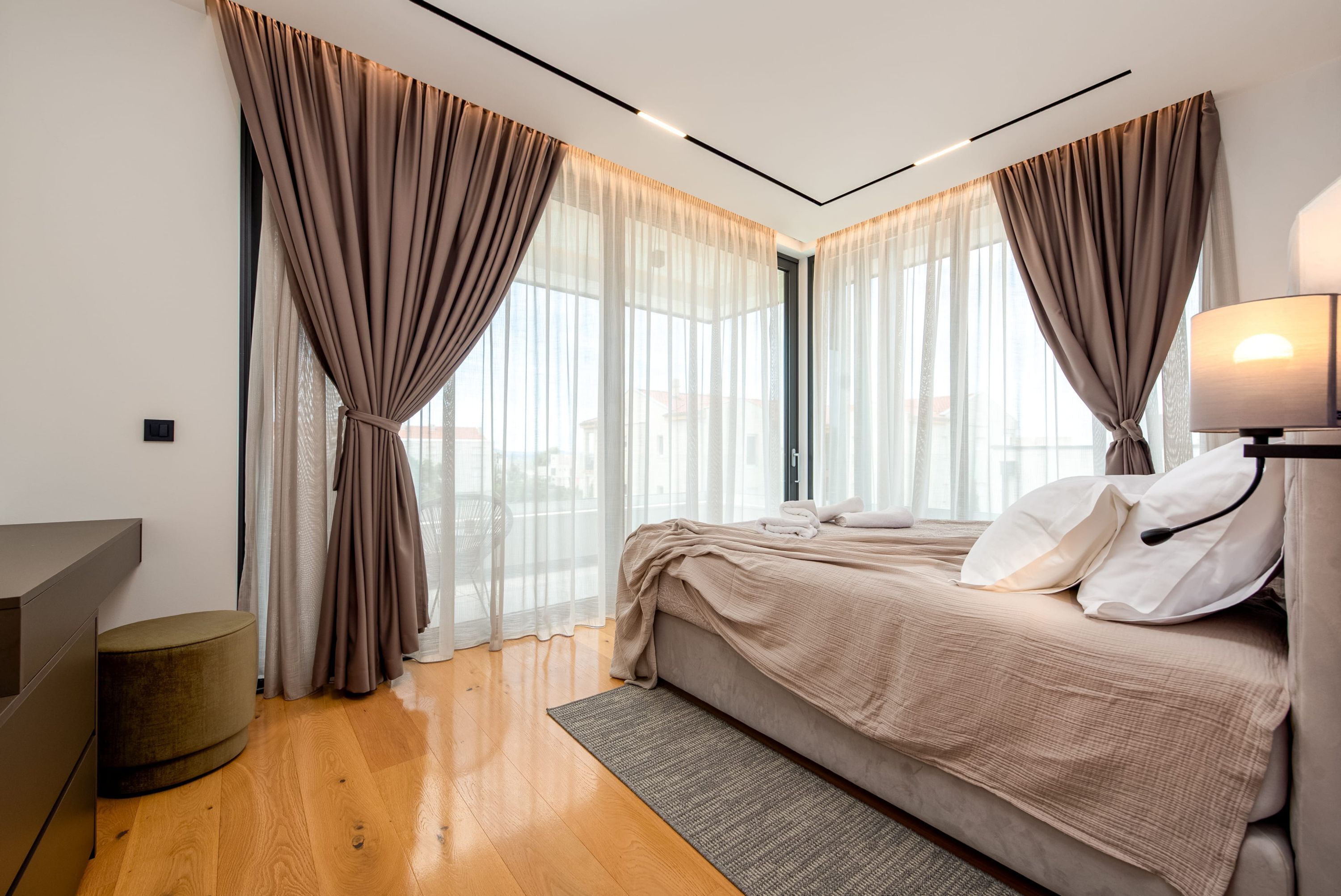 A modern bedroom with a bed, curtains, a desk, and a lamp.