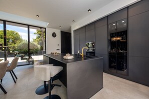 Una cocina moderna con una isla central, taburetes de bar y un ventanal con vistas a un jardín.