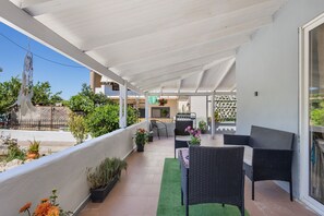 A covered outdoor patio with wicker furniture, potted plants, and a grill area. - Elena s House in Mournies (Chania)