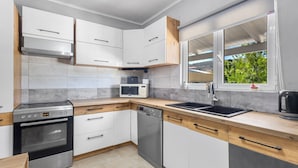 A modern kitchen with white cabinets, a stainless steel oven, a dishwasher, a microwave, and a window with a view of greenery. - Elena s House in Mournies (Chania)