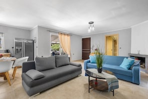 A modern living room with a grey sofa, a blue sofa, a dining area with a white table and chairs, and a kitchen with a stainless steel refrigerator. - Elena s House in Mournies (Chania)