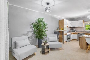 A modern kitchen with white cabinets, a microwave, and a dishwasher. There is a dining area with a table and chairs, and a large potted plant. - Elena s House in Mournies (Chania)