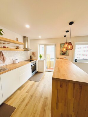 A modern kitchen with white cabinets, a wooden countertop, a built-in oven, and pendant lights. - Casa Mar - Beautiful apartment with an ocean view on Matosinhos Beach in Porto (Matosinhos)