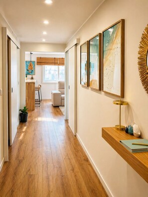 A hallway with wooden flooring, a kitchen area in the background, and a wall with framed artwork and a decorative mirror. - Casa Mar - Beautiful apartment with an ocean view on Matosinhos Beach in Porto (Matosinhos)