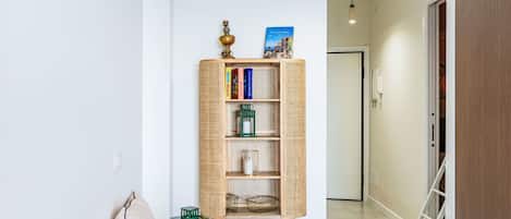 A hallway with a wicker bookshelf, a wicker chair, a white door, and a ladder.